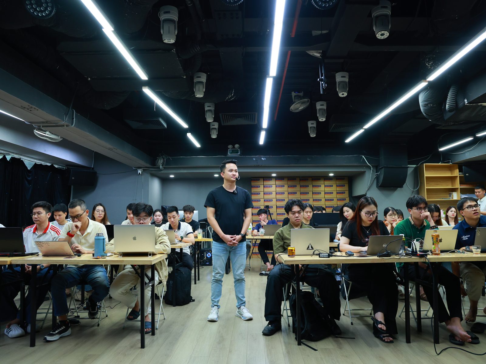 Phúc BANI đứng giữa hai dãy bàn, nhân viên mở laptop làm theo